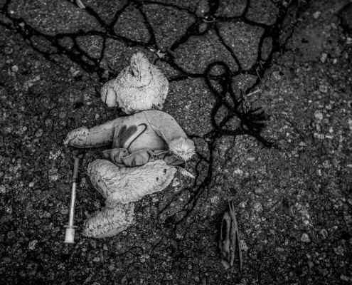 An abandoned stuffed bear is found beside a used syringe amongst the rubble of the dilapidated Packard Plant.